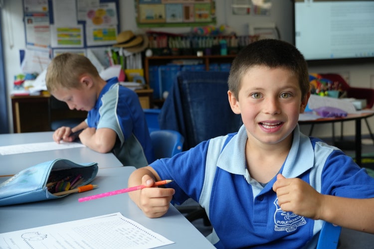 student sitting at desk with pencil in hand looking at the camera