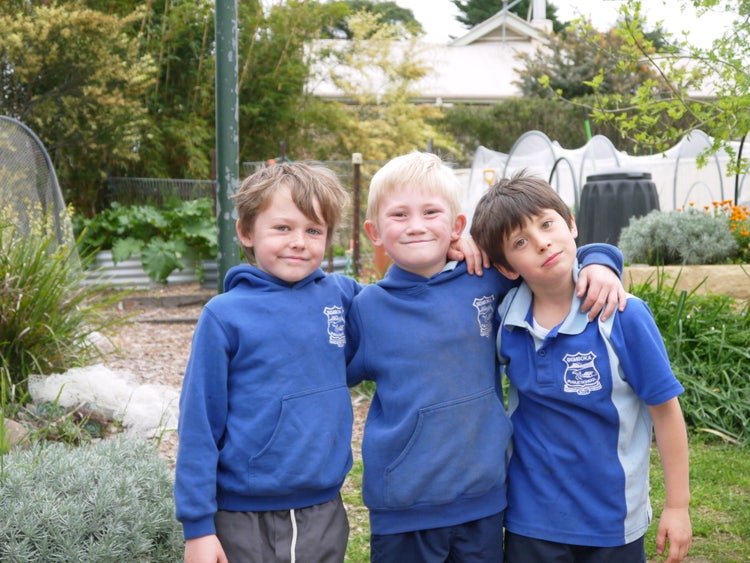 three students with arms around each other looking at camera with school garden in the background