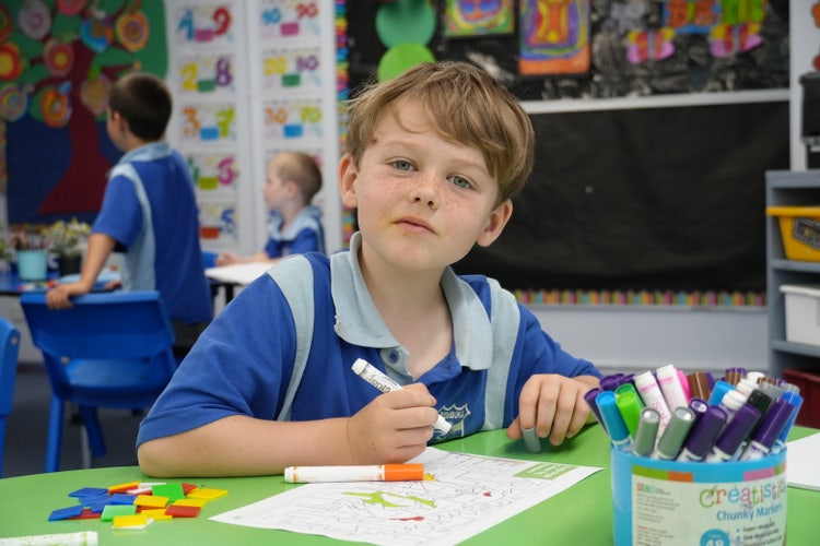 student sitting at desk colouring in looking at camera