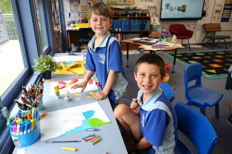 one student sitting one student standing working on art and craft